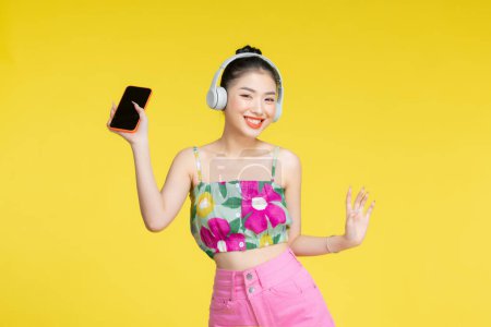 Foto de Feliz mujer asiática alegre con auriculares inalámbricos escuchando música desde el teléfono inteligente - Imagen libre de derechos