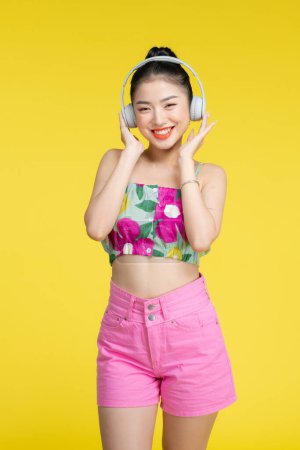 Téléchargez les photos : Jeune jolie femme asiatique portant des écouteurs écoutant de la musique et dansant - en image libre de droit