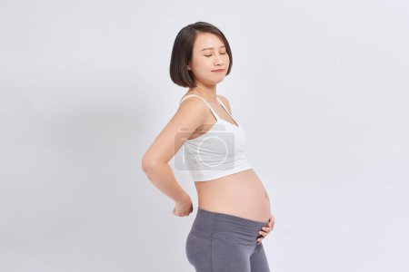 Photo for Young beautiful pregnant asian woman standing and touching belly and back - Royalty Free Image