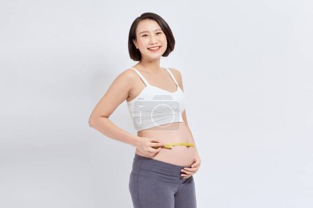 Téléchargez les photos : Portrait jeune femme enceinte heureuse mesurant l'estomac avec ruban à mesurer - en image libre de droit