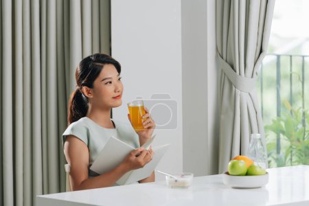 Photo for Young asian woman reading book and drinking orange juice at home - Royalty Free Image