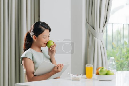 Téléchargez les photos : Une jeune femme heureuse assise à l'intérieur au salon tenant livre lecture boire du jus d'orange. - en image libre de droit