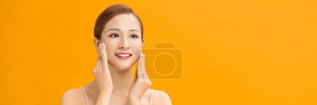Téléchargez les photos : Belle jeune femme asiatique nettoyer son visage avec des tampons de coton sur fond jaune, bannière - en image libre de droit