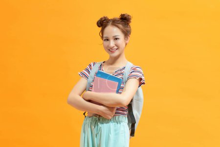 Foto de Joven estudiante con mochila sosteniendo libros sobre un fondo amarillo aislado. - Imagen libre de derechos
