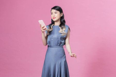 Téléchargez les photos : Jeune belle femme souriante en robe de soirée en soie bleue à la mode avec smartphone - en image libre de droit