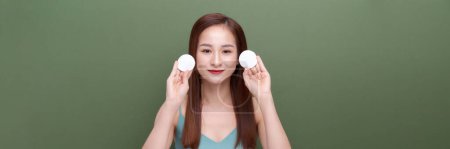 Foto de Atractivo sonriente asiático mujer limpieza piel en verde banner fondo - Imagen libre de derechos