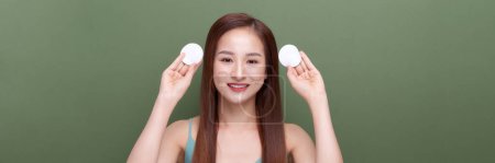 Téléchargez les photos : Positive asiatique femme tenue coton pad près du visage isolé sur vert, panorama, culture - en image libre de droit
