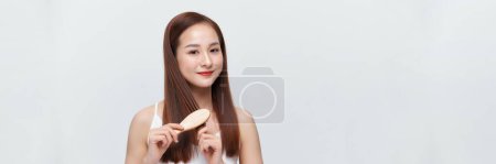 Photo for Banner of young asian woman brushing her hair and smiling, isolated over white background - Royalty Free Image