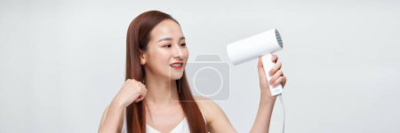 Téléchargez les photos : Portrait d'une jeune femme asiatique utilisant un sèche-linge sur fond de bannière blanche - en image libre de droit
