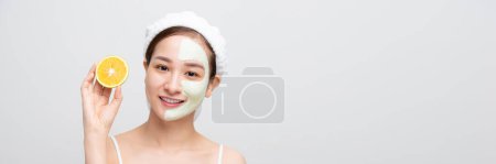 Téléchargez les photos : Femme asiatique souriante avec tranche d'orange et masque de boue sur le visage pour bannière web - en image libre de droit