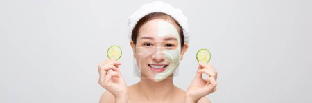 Téléchargez les photos : Belle jeune femme asiatique avec masque facial concombre sur fond blanc. Bannière - en image libre de droit