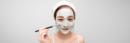 Téléchargez les photos : Heureux asiatique femme avec une serviette sur son tête appliquer un nettoyage masque sur son visage - en image libre de droit