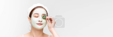 Téléchargez les photos : Portrait de femme asiatique appliquant un masque nourrissant blanc ou crème sur le visage, feuille verte à la main. bannière - en image libre de droit