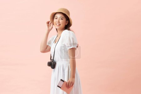 Téléchargez les photos : Heureuse femme touristique portant un chapeau avec caméra, passeport isolé sur fond rose - en image libre de droit