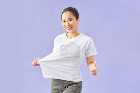 Foto de Probando camiseta después de una dieta fuerte aislada sobre fondo violeta - Imagen libre de derechos