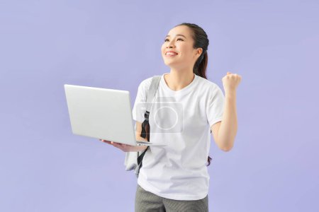 Téléchargez les photos : Jeune étudiante sac à dos tient ordinateur portable isolé sur fond violet mur studio portrait. - en image libre de droit