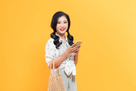 Photo for Happy asian girl using mobile phone standing over yellow background with copy space - Royalty Free Image
