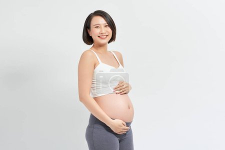 Foto de Hermosa asiático embarazada mujer holding su vientre en blanco fondo - Imagen libre de derechos