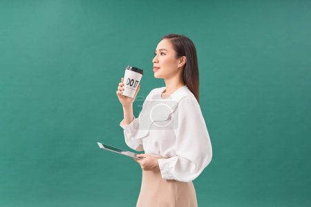 Photo for Young woman holding digital tablet and paper cup isolated on green - Royalty Free Image