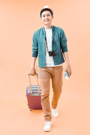 Foto de Feliz asiático viajero masculino caminando con maleta contra fondo de color - Imagen libre de derechos