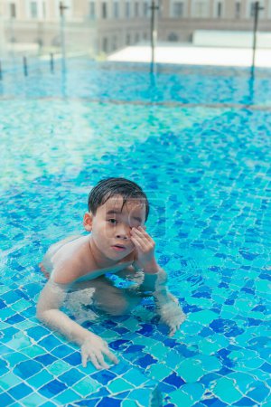 Téléchargez les photos : Enfant sur les marches de la piscine, frottant l'eau de ses yeux. - en image libre de droit