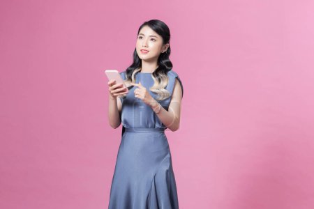 Photo for Beautiful young asian woman using smart phone isolated on pink - Royalty Free Image