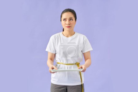 Photo for Young woman holding yellow measuring tape as dieting symbol and weight scales - Royalty Free Image