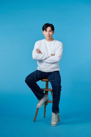 Photo for Handsome young man sitting on the chair, isolated on blue background - Royalty Free Image