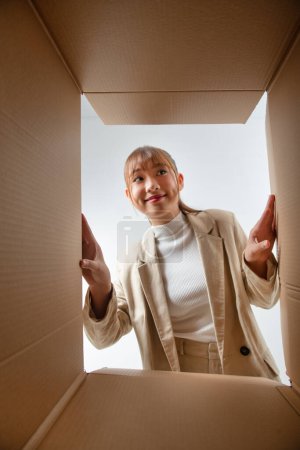 Téléchargez les photos : Joyeux asiatique jeune femme ouverture boîte en carton ou colis et regarder à l'intérieur - en image libre de droit