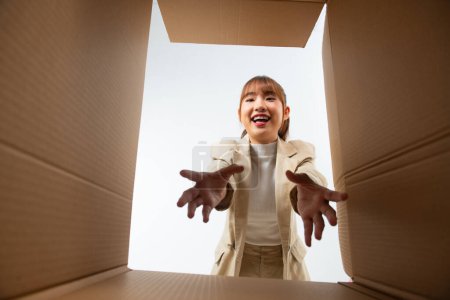 Foto de Emocionado mujer asiática desempacando, abriendo caja de cartón y tratando de conseguir algo, vista desde el interior - Imagen libre de derechos