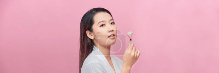 Téléchargez les photos : Belle asiatique femme massage visage avec jade rouleau isolé sur fond rose - en image libre de droit