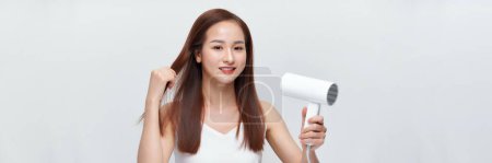 Foto de La mujer seca su hermoso cabello largo con un secador de pelo sobre un fondo blanco. Banner web - Imagen libre de derechos