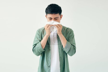 Téléchargez les photos : Jeune homme essuyant son nez avec un mouchoir sur fond blanc - en image libre de droit