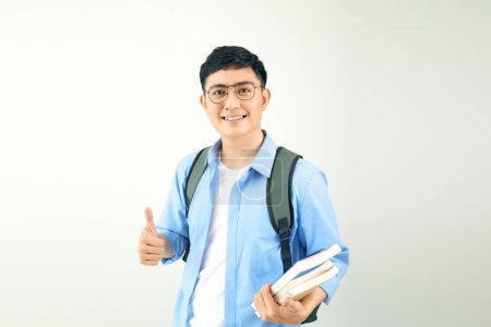 Téléchargez les photos : Jeune étudiant souriant tenant des livres portant un sac à dos, isolé sur un fond blanc. - en image libre de droit