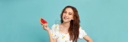 Téléchargez les photos : Femme souriante tenant et mangeant tranche de pastèque fraîche sur fond bleu - en image libre de droit