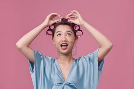 Photo for Headshot of a young woman with hair curlers over pink background - Royalty Free Image