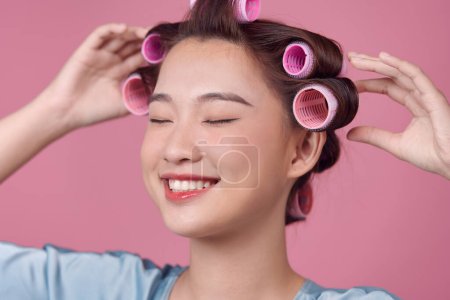 Téléchargez les photos : Belle jeune femme en rouleaux de cheveux sur fond rose - en image libre de droit