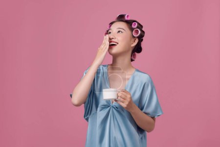Téléchargez les photos : Femme en rouleaux de cheveux avec une tasse de café sur un fond rose - en image libre de droit