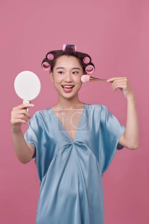Photo for Pretty woman with curlers on hair, holding makeup brush and mirror in hands - Royalty Free Image