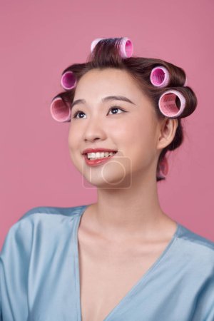 Foto de Joven hermosa chica teniendo rulos de pelo en su cabeza aislado sobre fondo rosa - Imagen libre de derechos