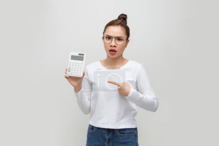 Foto de Mujer de negocios con clase preocupada sobre fondo blanco que sostiene la calculadora - Imagen libre de derechos