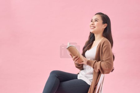 Photo for Beautiful woman sitting on pink background and reading a book - Royalty Free Image