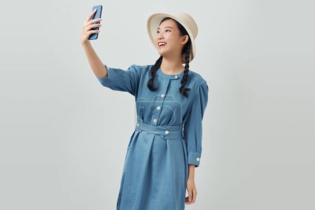 Foto de Asiático chica posando aislado en blanco fondo haciendo selfie disparo en móvil difusión manos - Imagen libre de derechos