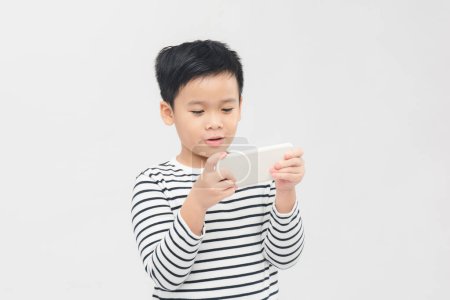 Téléchargez les photos : Petit garçon sérieux utilisant un smartphone sur fond de bannière blanche. - en image libre de droit