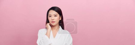 Foto de Hermosa chica asiática modelo con maquillaje natural tocando brillante piel hidratada sobre fondo rosa, panorama - Imagen libre de derechos