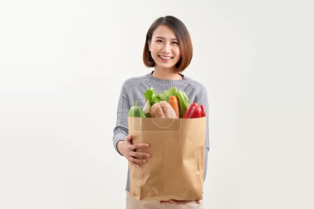 Photo for Smiling woman holding a shopping bag full of groceries posing on a studio white background. - Royalty Free Image