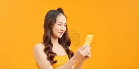 Foto de Mujer joven sonriente usando el teléfono móvil contra fondo amarillo vivo, panorama - Imagen libre de derechos