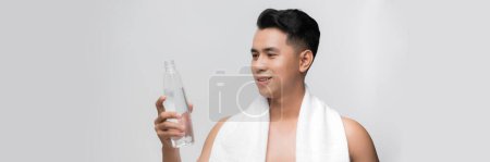Téléchargez les photos : Jeune homme confiant avec serviette sur les épaules tenant la bouteille avec de l'eau et souriant - en image libre de droit