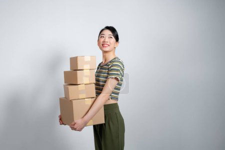 Foto de Feliz chica asiática sosteniendo paquetes de cajas aisladas sobre fondo gris. - Imagen libre de derechos