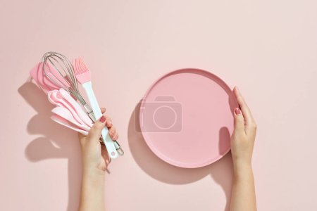 Foto de Woman hand holding kitchen utensils on pink background. Baking tools - Imagen libre de derechos